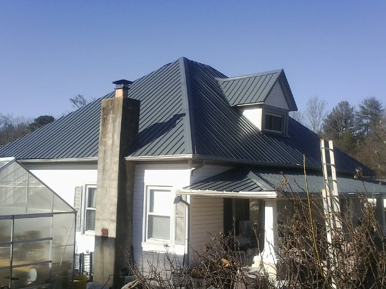 Dark blue standing seam metal roof on a white farmhouse with dormer — Slate & Tile Roof Repair by Roofing Brothers in Lafferty