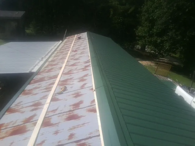 Old rusted panels beside newly installed green metal roofing — Wind Damage Roof Repair by Roofing Brothers in Lafferty