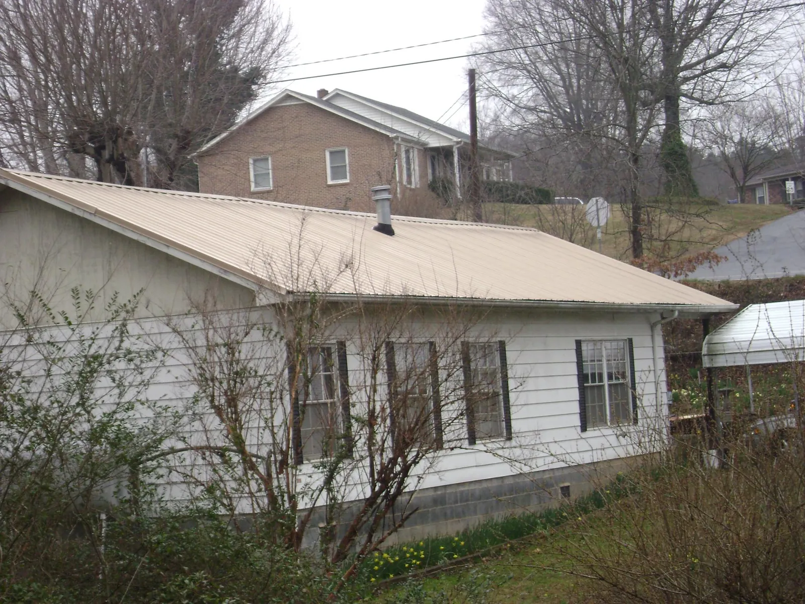Tan metal roof on a white sided house set into a hillside — Commercial Roofing by Roofing Brothers in Lafferty