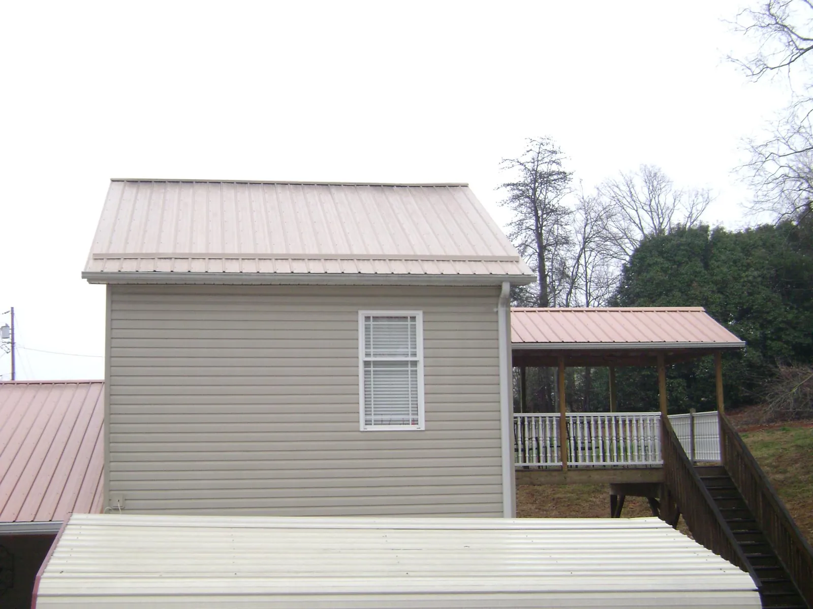 Tan metal roofs on a two story addition and attached porch, from a Roof Replacement job in Lafferty